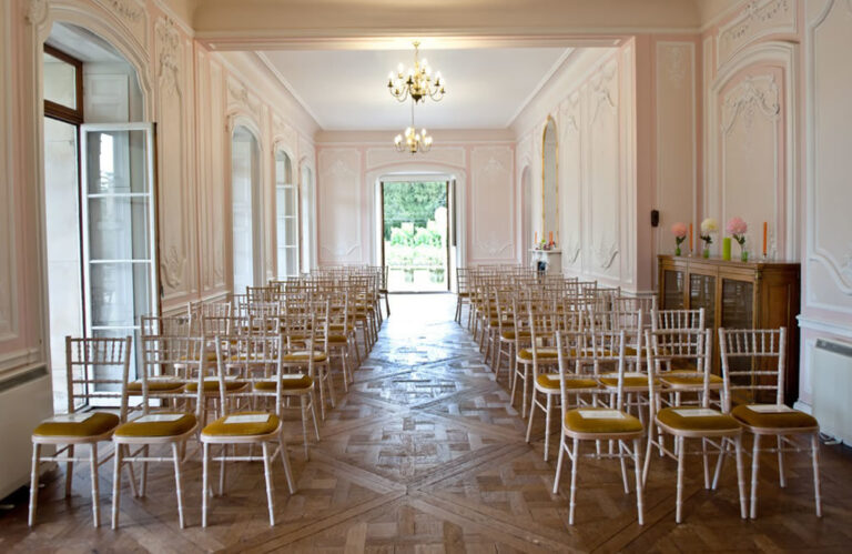 Long gallery room set for a ceremony with gold chiavari chairs and a chandelier.