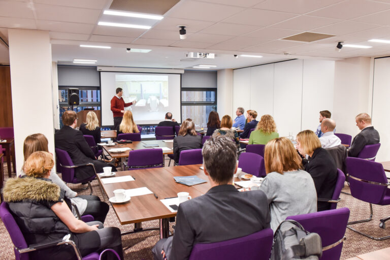 Presenter at a whiteboard with delegates seated around a table