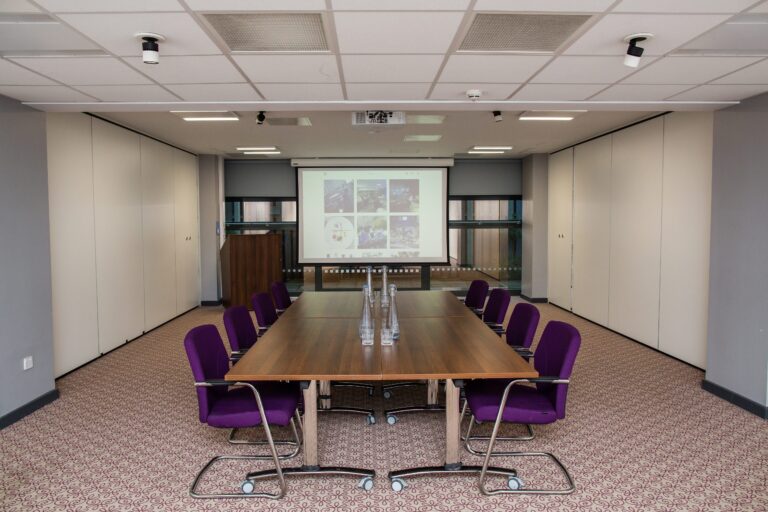INOX Suite boardroom table with purple chairs and a wall screen