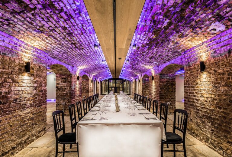 London Bridge Arches with a long table beneath purple-lit brick vaults