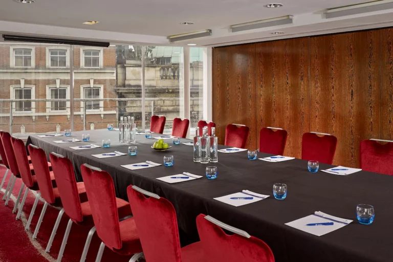 Boardroom with a long table, wood-panelled wall and a view of brick buildings.
