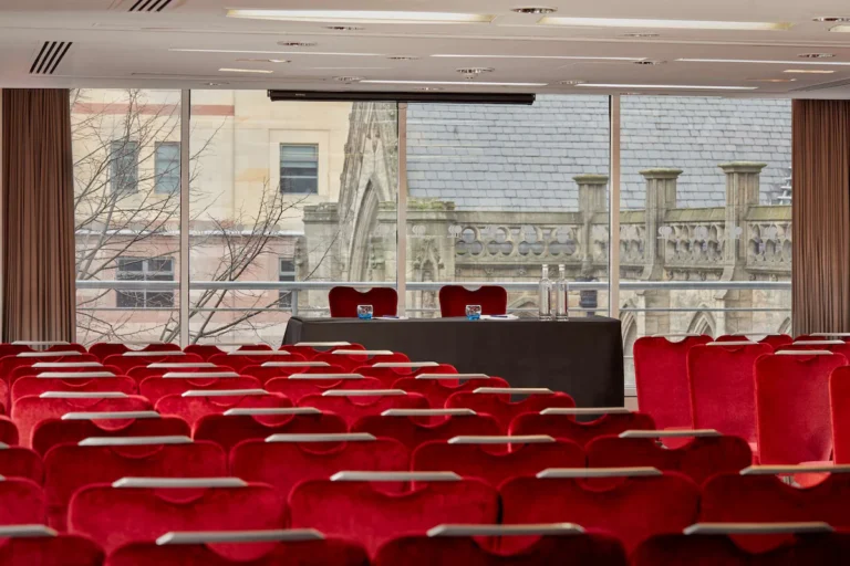 Theatre-style meeting room with rows of red velvet chairs facing a screen and a gothic church view.