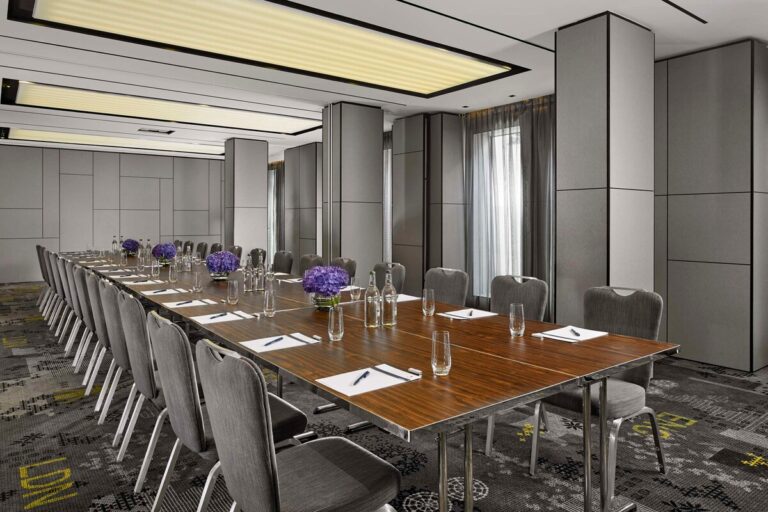 Boardroom-style meeting room with a long table, purple flower arrangements and grey panelled walls.