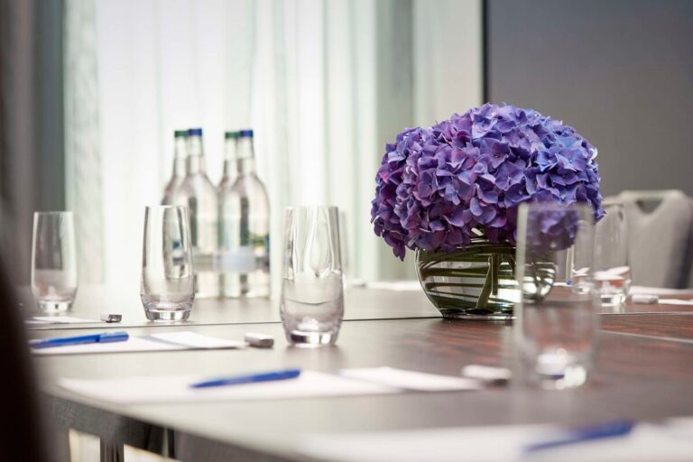 Close-up of a purple hydrangea centrepiece on a meeting table with water glasses and notepads.