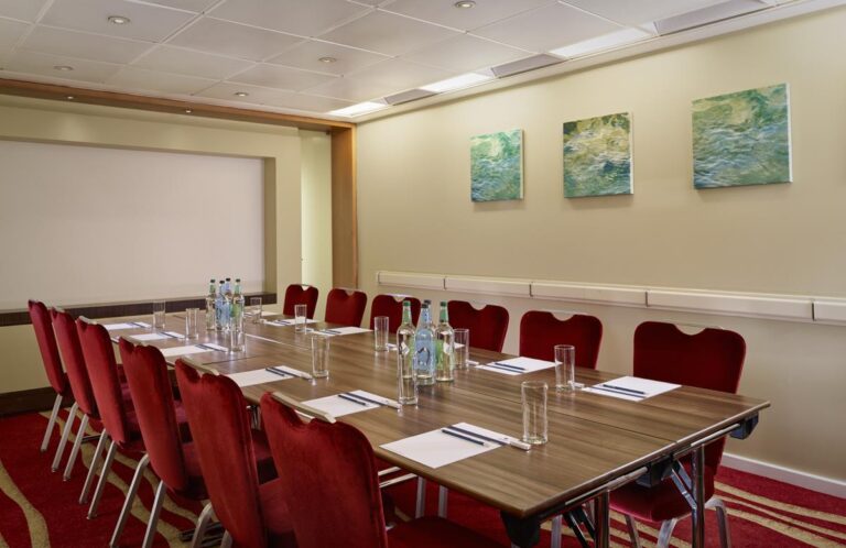Boardroom with a long table, red velvet chairs and green abstract artwork on the walls.