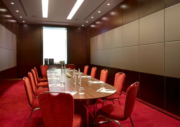 Plaza Suite oval boardroom table with red chairs and dark wood panelling