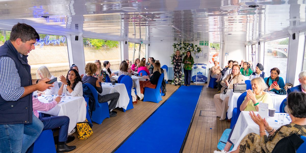 Guests seated at tables along a blue carpet aisle applauding on the boat