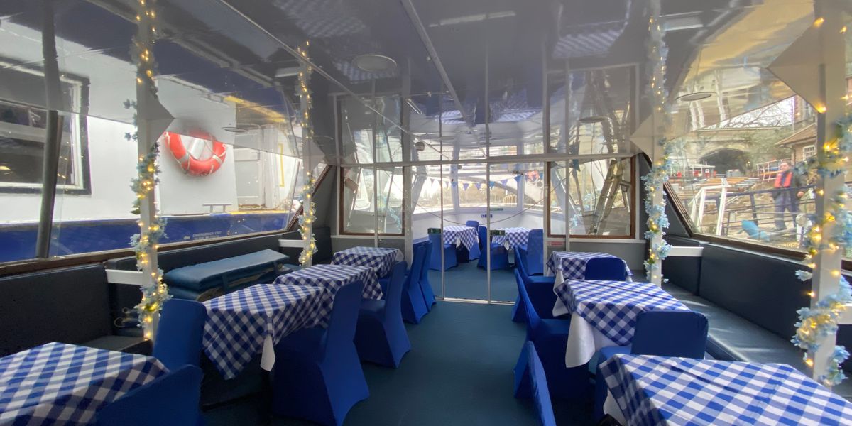 Boat dining saloon with blue-checked tablecloths beside large windows