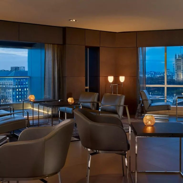 River view lounge with grey armchairs, tea light candles and a night-time view of Westminster.