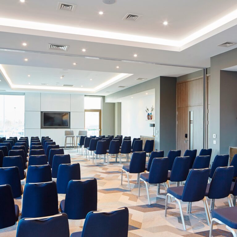 Conference room set theatre-style with rows of blue chairs and a wall screen