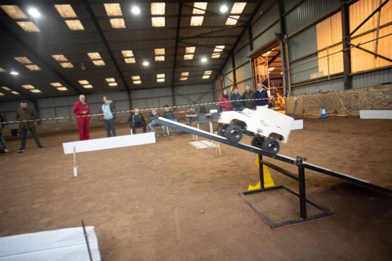 Indoor arena with a dirt floor where a small vehicle is being tested