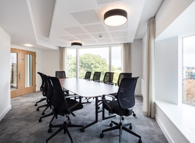 Tulip Boardroom with a long white table, black mesh chairs and a tree-lined window view.