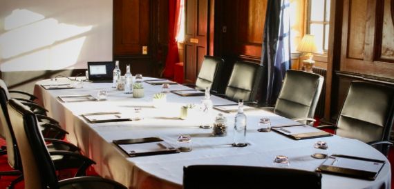 Wood-panelled boardroom with an oval table, black leather chairs and window views