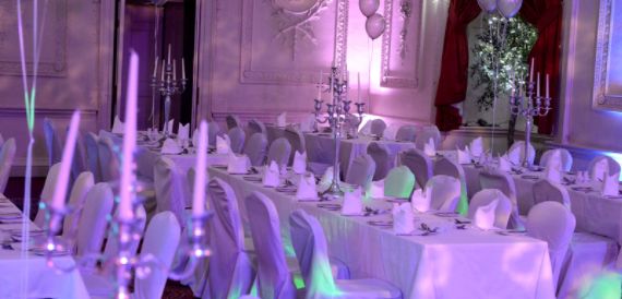 Wedding reception room dressed in purple lighting with white chair covers and candelabras