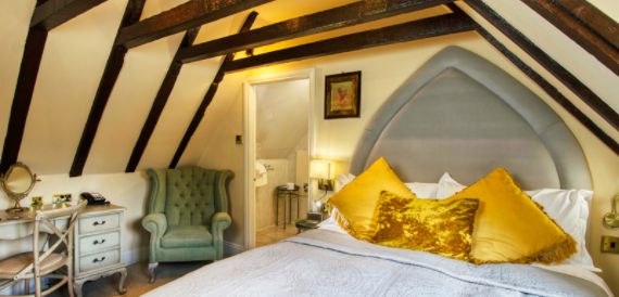 Bedroom with exposed timber beams, a gothic-arched headboard and gold cushions