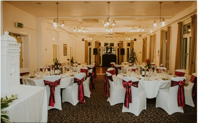 Function room set for a wedding with round tables and red chair sashes