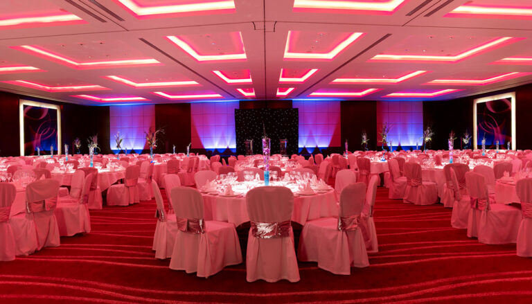 Wide view of the ballroom set with round tables and pink uplighting