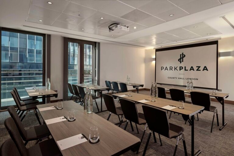Westminster boardroom set up with a U-shaped table, red chairs and blue curtains.