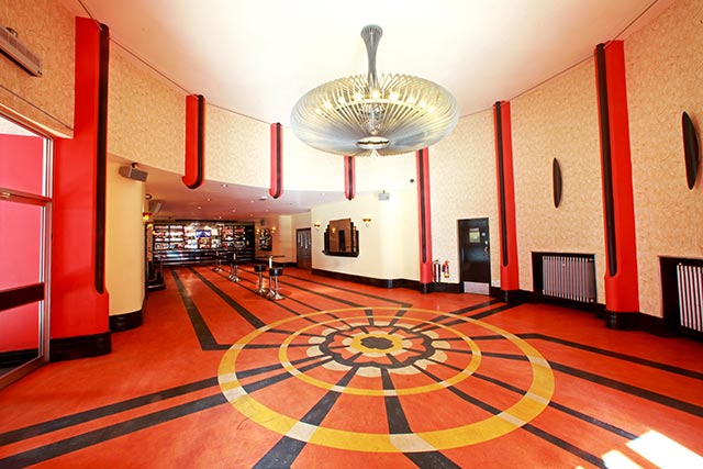 Art deco foyer with red pillars, a patterned floor and ornate chandelier
