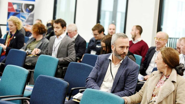 Audience seated in teal chairs listening to a conference talk
