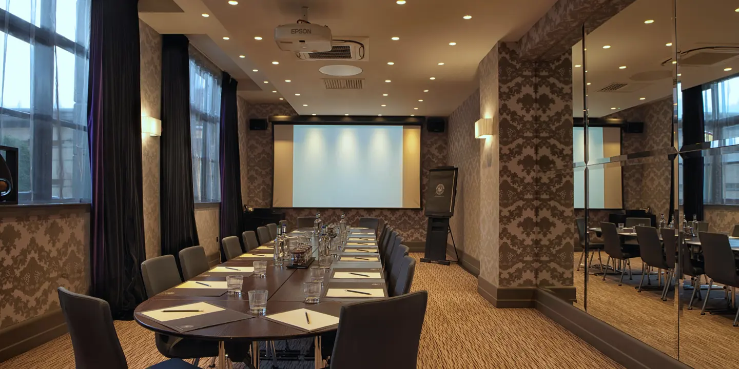 Boardroom set theatre-style with a long table, projector screen and mirrored wall