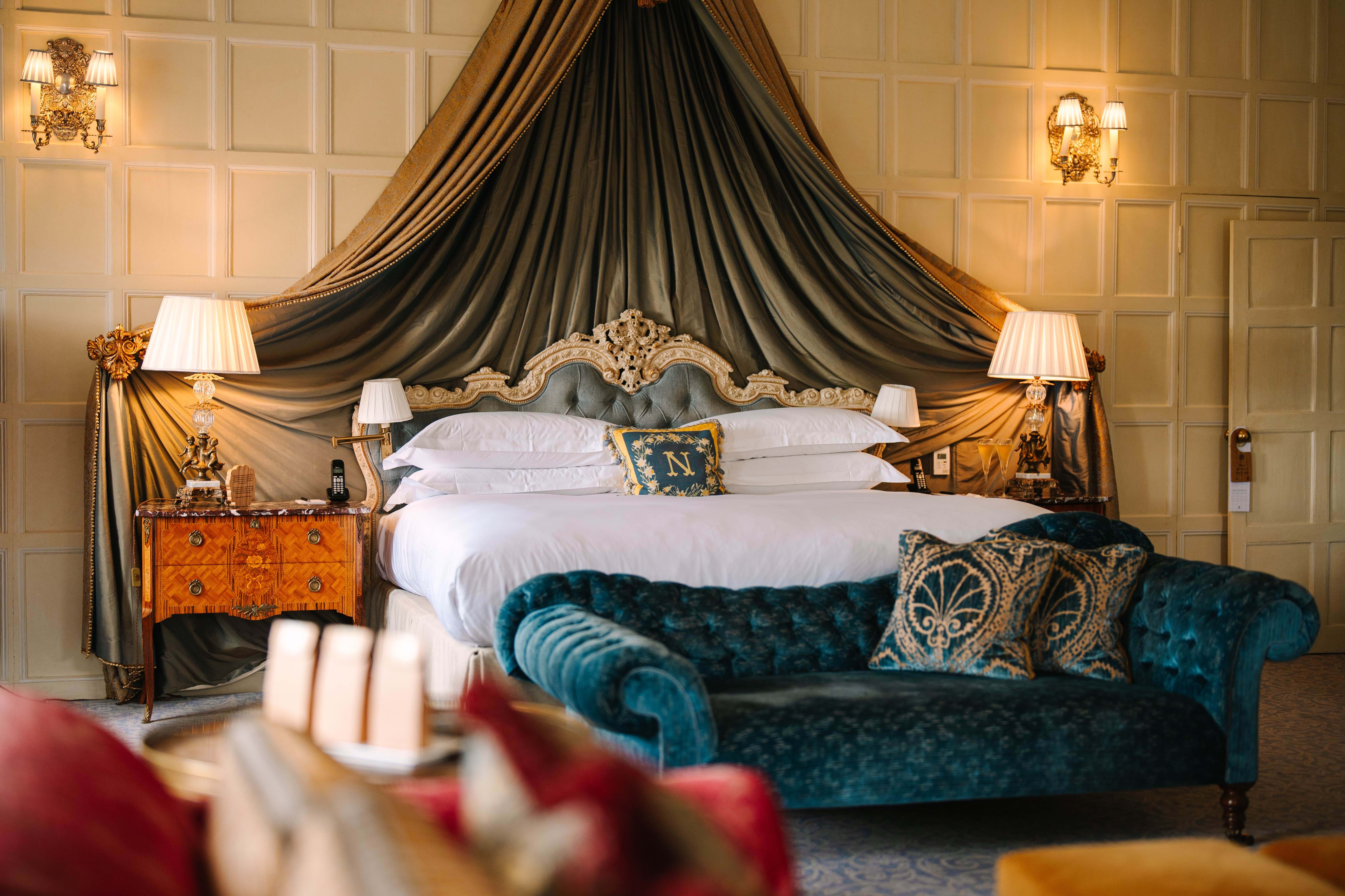 Cliveden bedroom with a canopy bed, ornate carved headboard and teal chaise longue