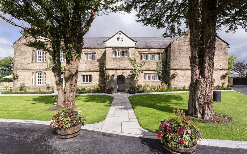 Stone manor house exterior at Haighton Manor with a lawned entrance and trees.