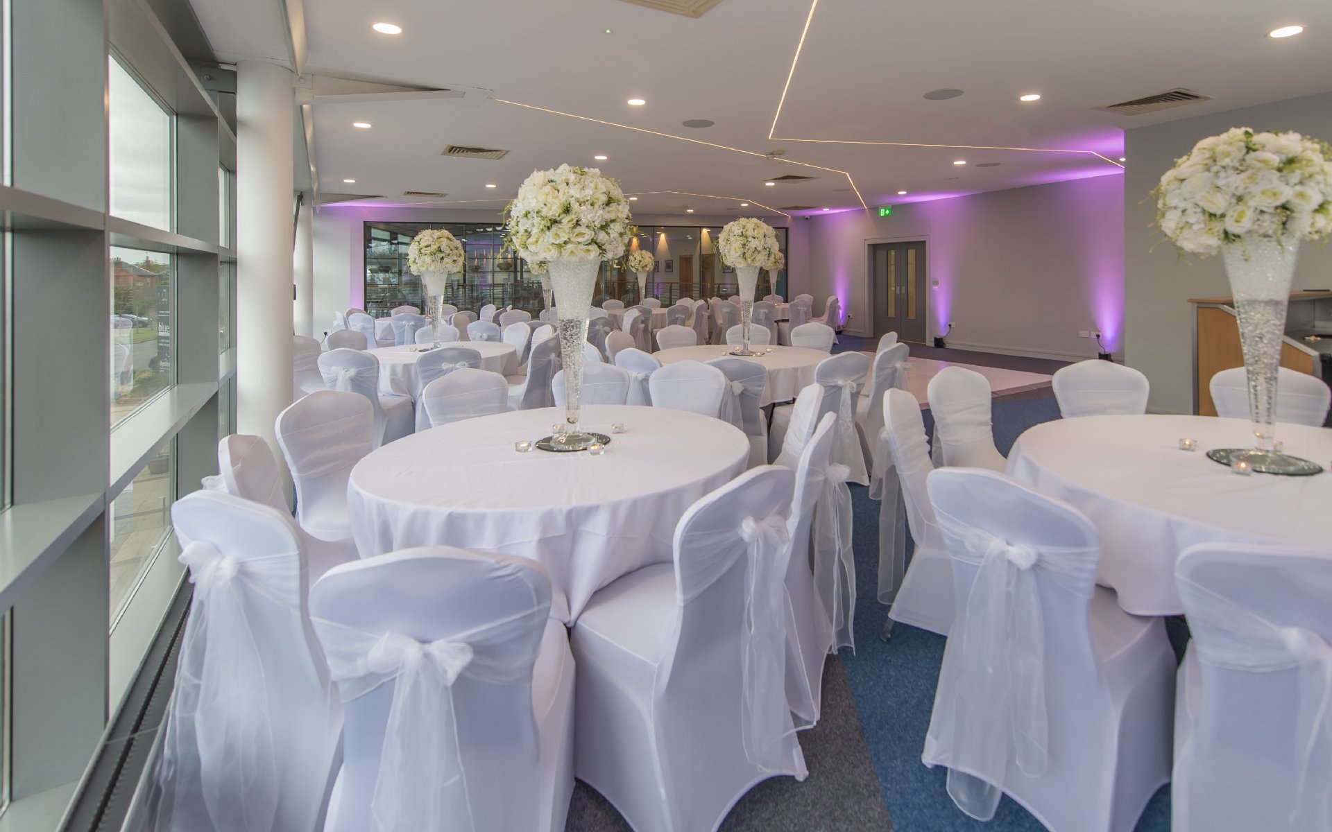 Wedding reception room with round tables, white chair covers and tall floral centrepieces