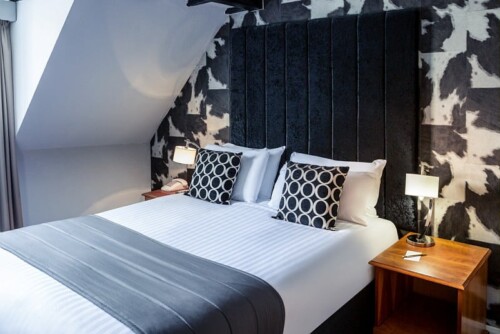 Bedroom with a black tufted headboard, patterned wallpaper and bedside lamps.