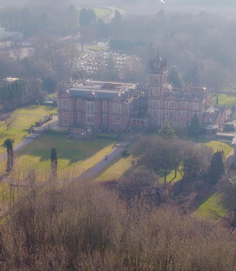 Aerial view of Crewe Hall's red brick facade surrounded by parkland and mature trees