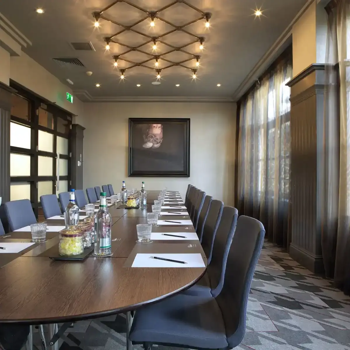 Boardroom table with a geometric light fixture overhead and framed artwork on the wall