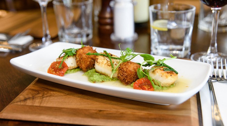 Seared scallops with black pudding, pea puree and cherry tomatoes on a plate.