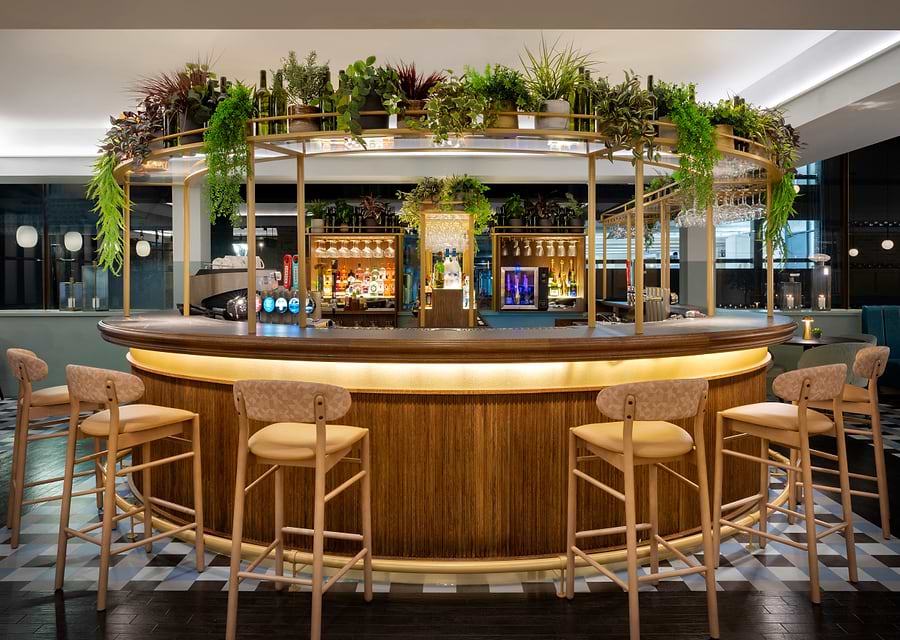 Round bar counter backlit with warm lighting beneath a canopy of greenery