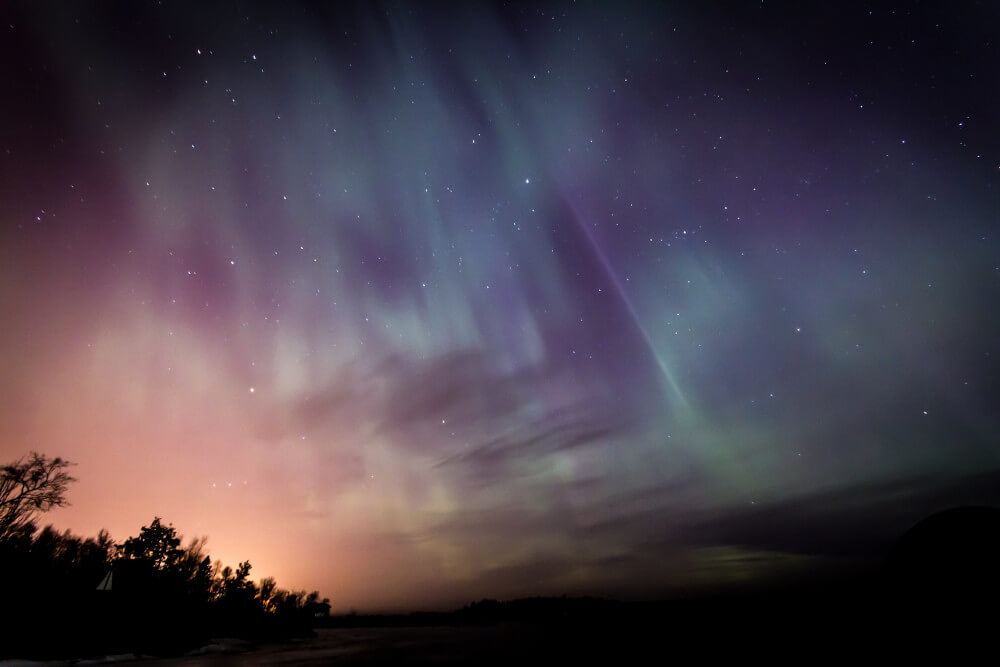 Colourful aurora borealis glowing green and purple over a dark landscape