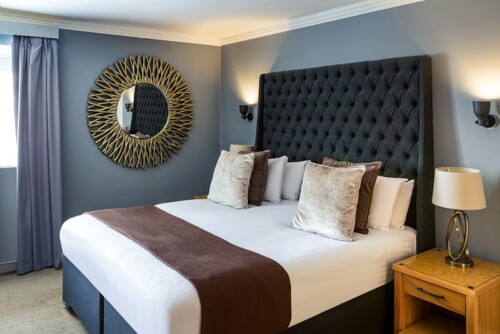 Bedroom with a round sunburst mirror, grey walls and a brown throw on the bed.