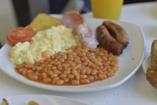 Full English breakfast plate with baked beans, scrambled egg, bacon and sausage.