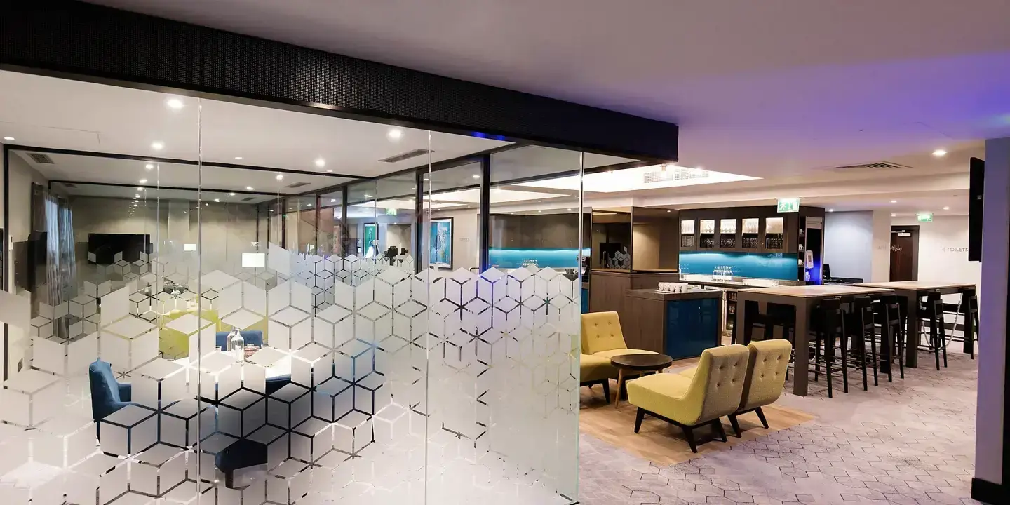Hotel lounge and bar with a glass-panelled meeting room, yellow armchairs and a poseur table