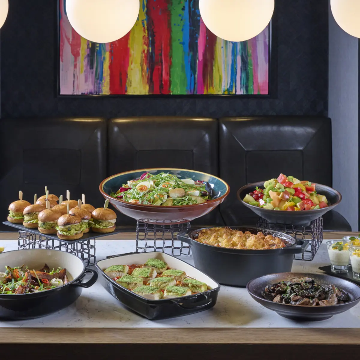 Buffet spread of sliders, salads, tray bakes and desserts on a wooden table