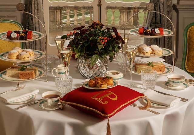Afternoon tea stand with pastries beside a red monogrammed cushion