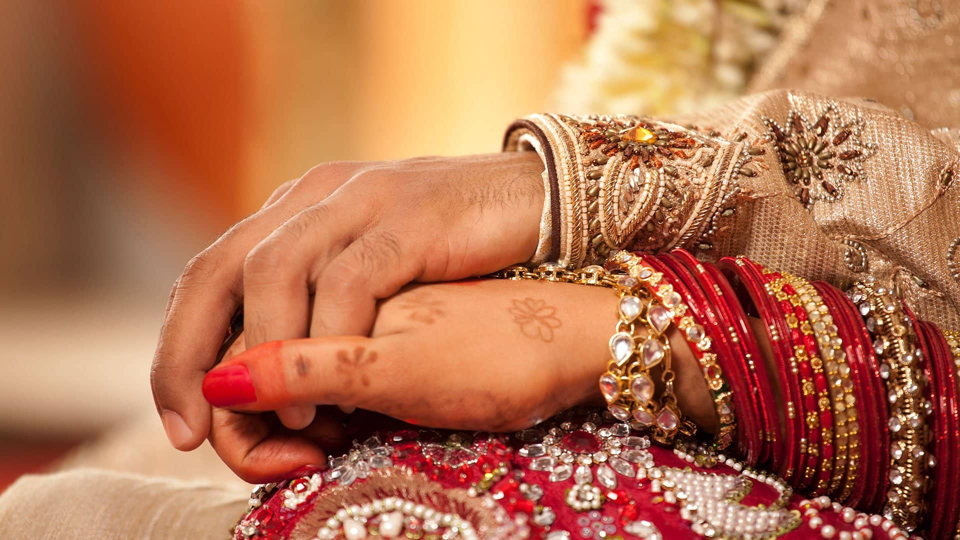 Close-up of a bride and groom's hands adorned with bangles and mehndi