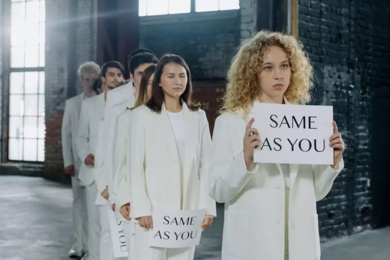 Group of people in white outfits holding signs reading same as you
