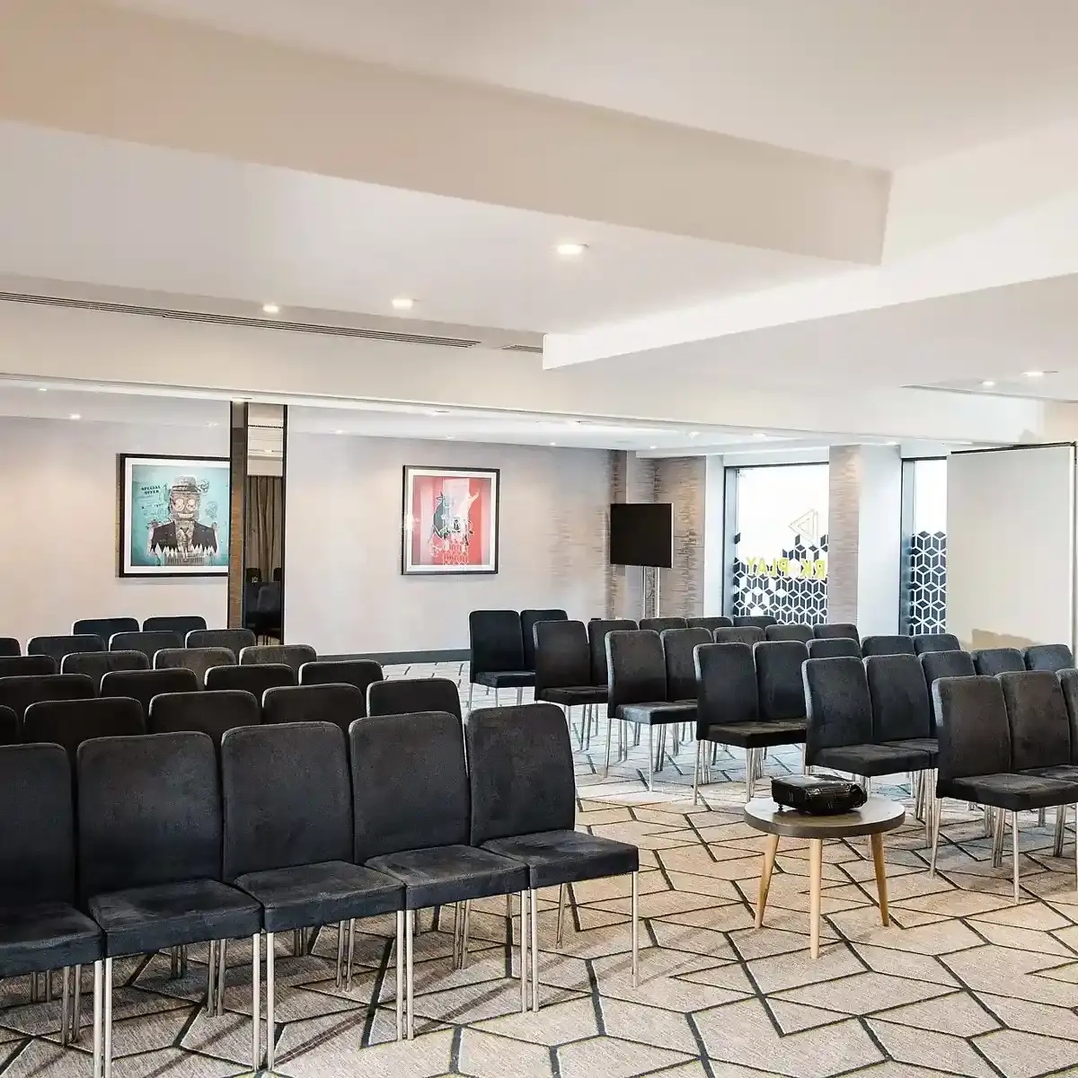 Meeting room set theatre-style with rows of dark chairs facing a wall-mounted screen