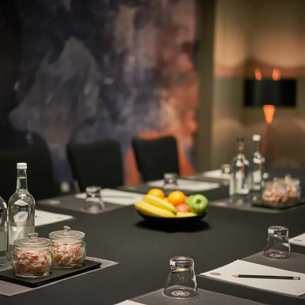 Boardroom table set with a fruit bowl, water bottles and sweet jars beside a screen