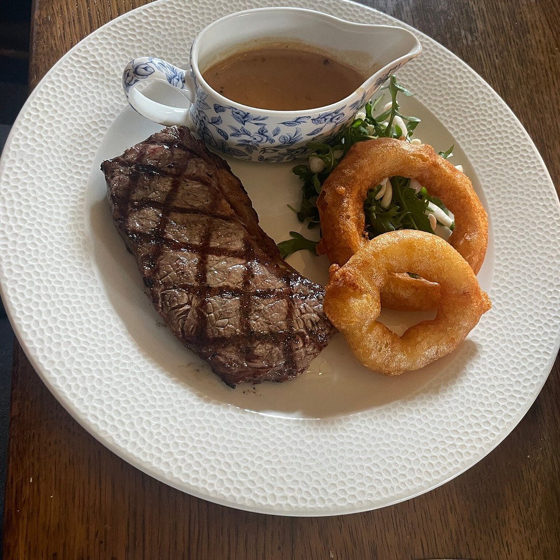 Grilled steak with onion rings, rocket salad and a jug of gravy.