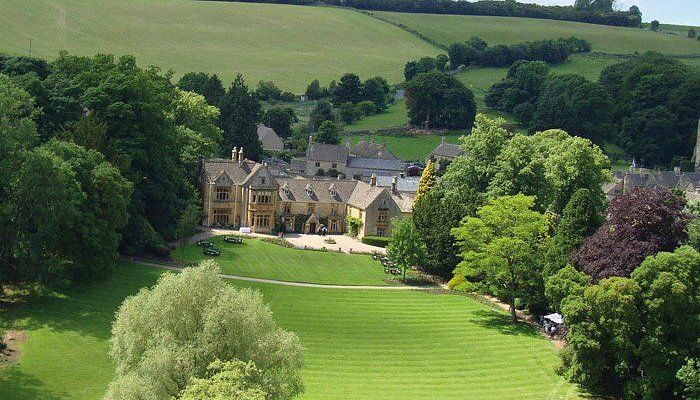 Aerial view of Lords of the Manor's stone facade set among lawns and woodland