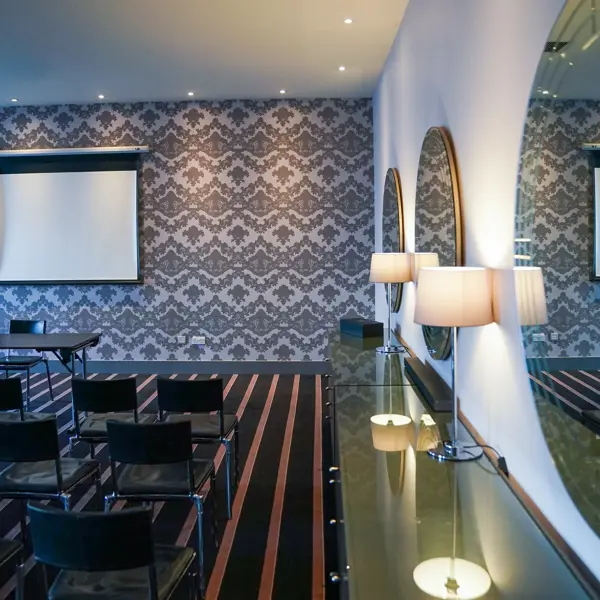 Meeting room with rows of chairs facing a projector screen beside a mirrored wall