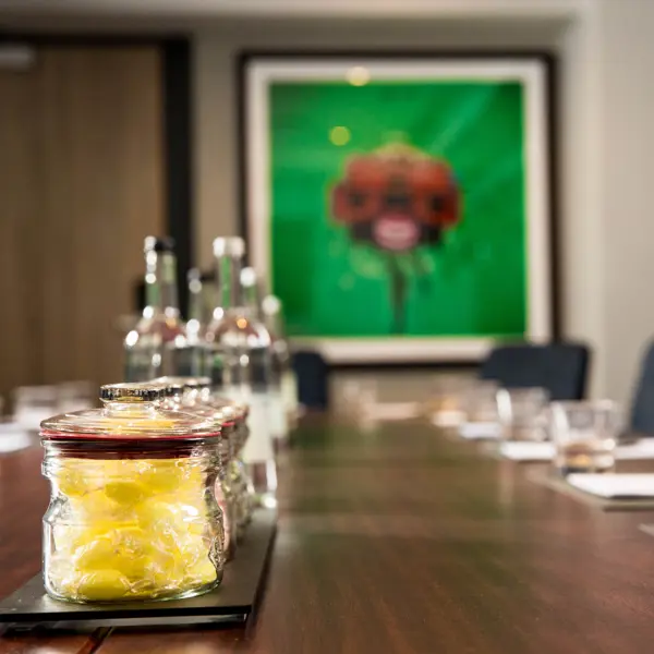 Close-up of sweet jars and water bottles on a boardroom table beside colourful artwork