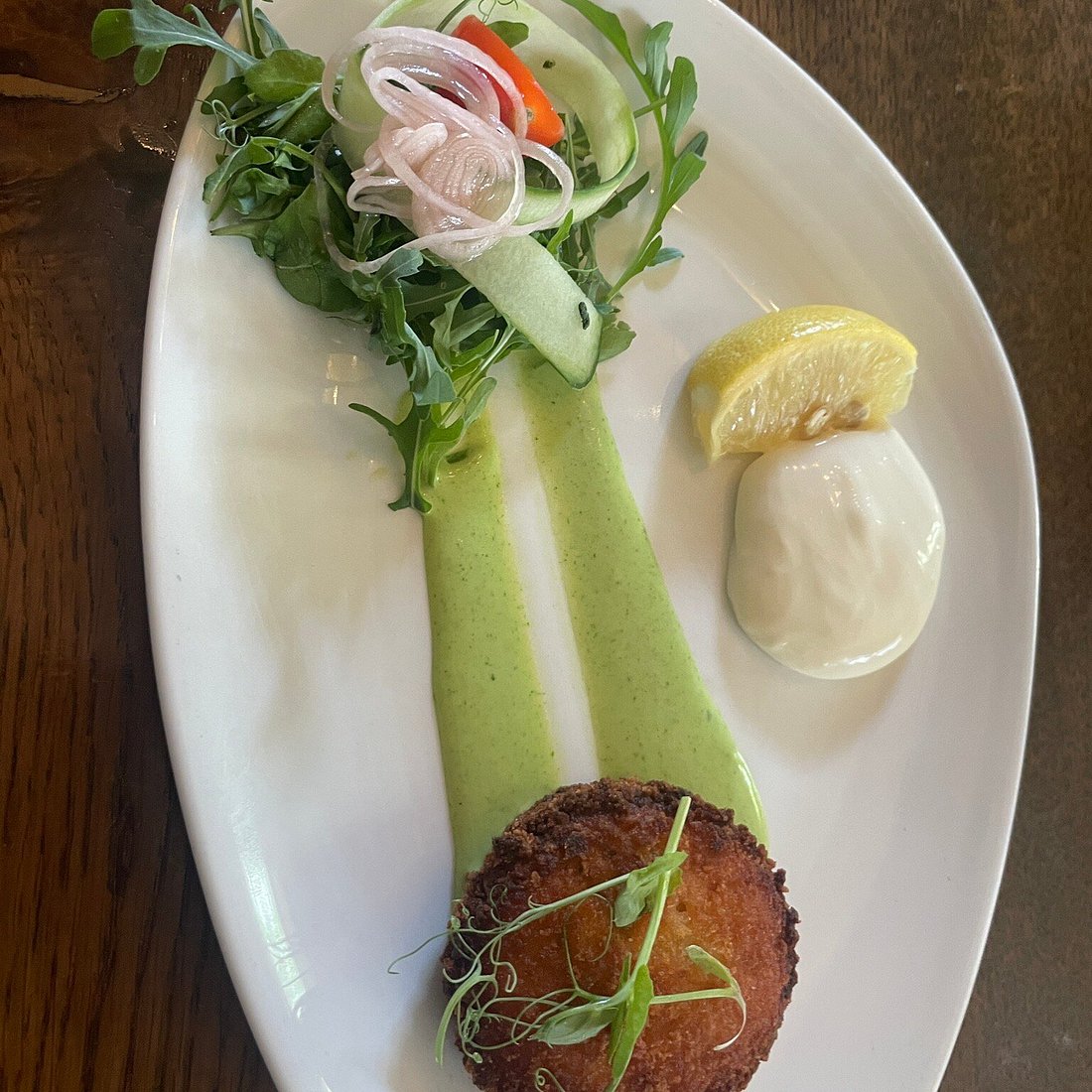 Fishcake with pea puree, pickled shallot salad and a lemon wedge.