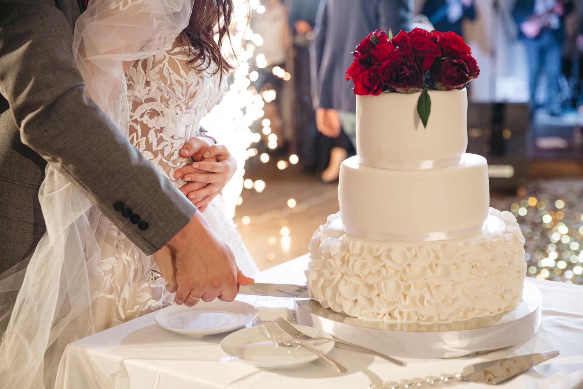 Bride and groom cutting a white wedding cake topped with red roses