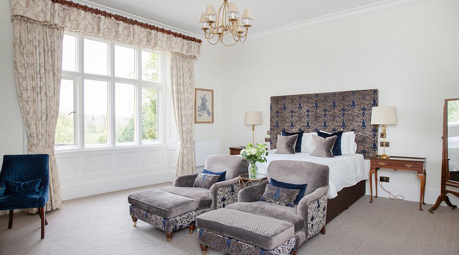 Hotel bedroom with a four-poster style bed, patterned armchairs and a large window